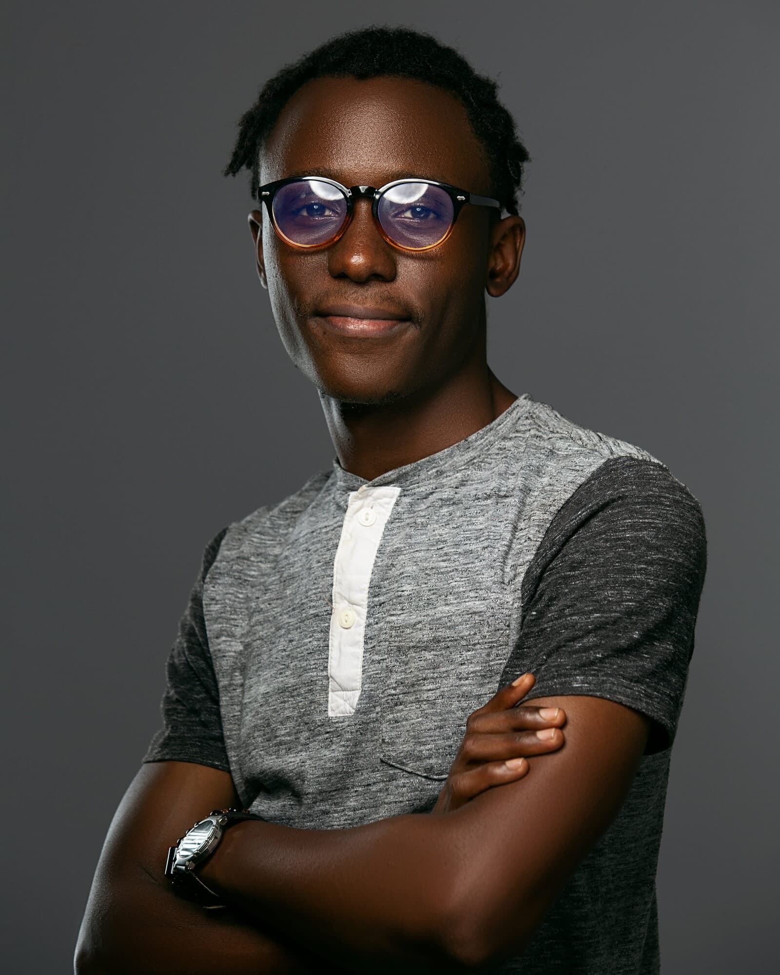 Layò smiling with arms folded, wearing round glasses and a grey henley